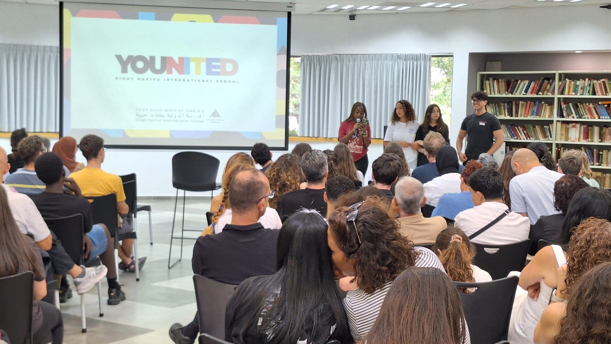 students standing with microphone in front of a presentation facing an audience