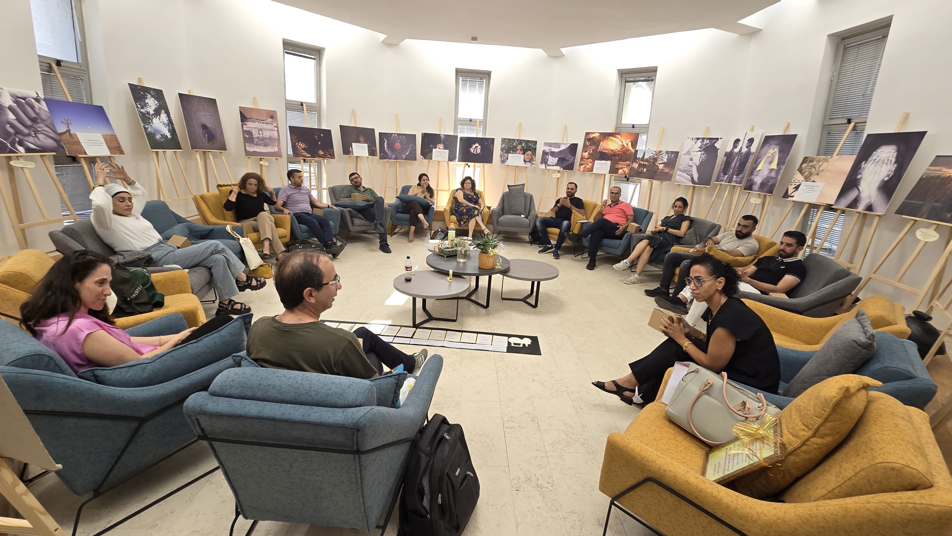 A group of people sitting around in a big circle with artwork hanging up on the wall